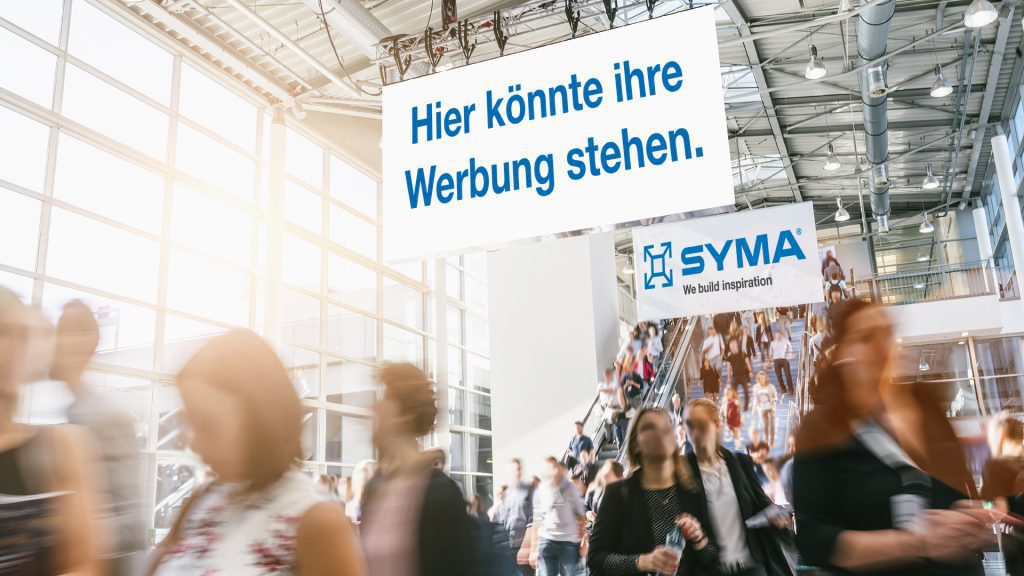 Lively exhibition hall with large SYMA posters for trade fair marketing