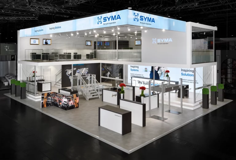 Gesamtansicht des SYMA-Messestands auf der EuroShop 2017, zweistöckiger Aufbau mit Präsentationsflächen und Lounge-Bereich.