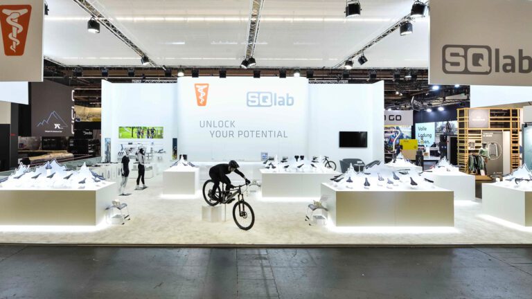 SQlab-Messestand auf der EUROBIKE mit Fahrradzubehör, modernen Displays und einem Fahrradfahrer.